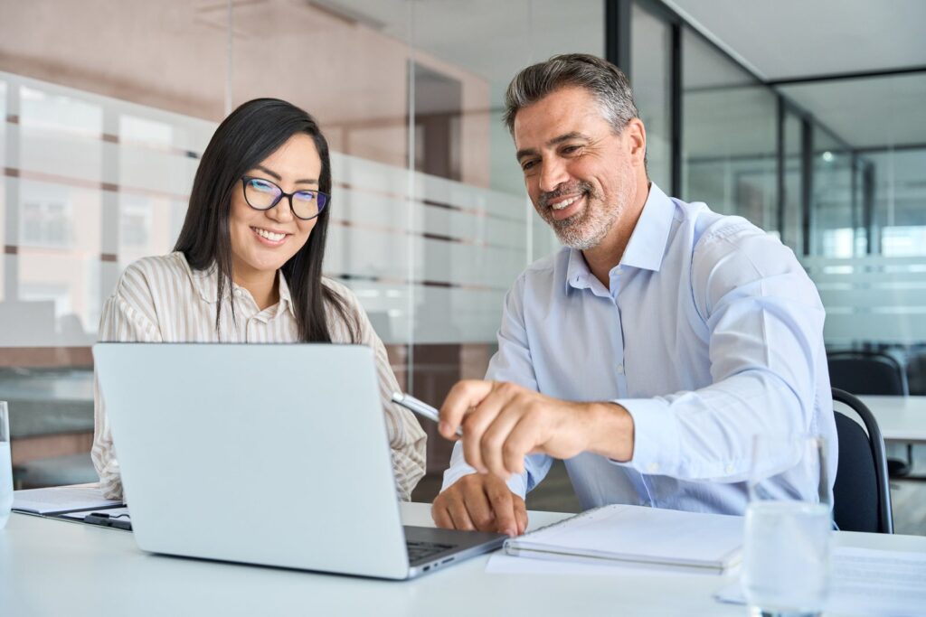 Duas pessoas conversando diante de um notebook em uma sala de reunião