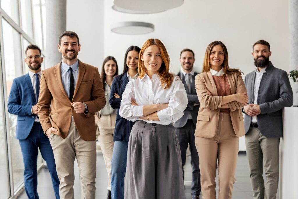Grupo de profissionais em pé, sorrindo, em um ambiente corporativo